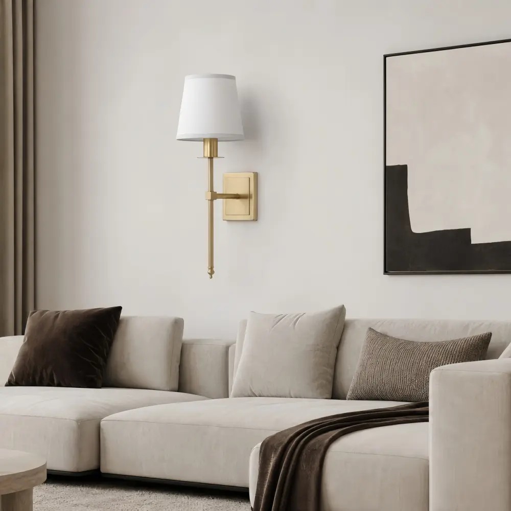 Een messing wandlamp met enkele kop boven een lichte bank in een warme woonkamer.