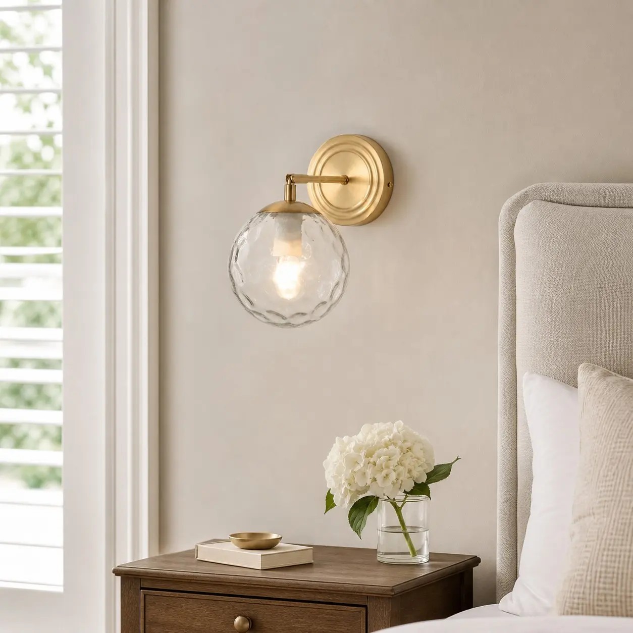 Lámpara de pared de cristal ondulado en un dormitorio de tonos neutros cálidos.