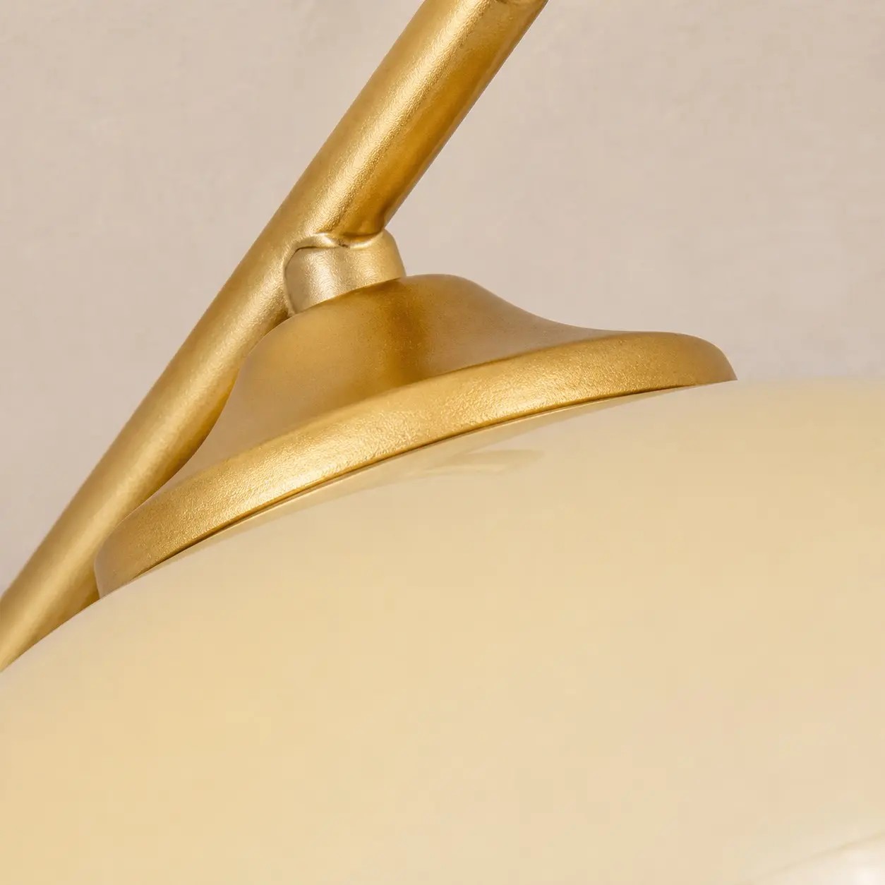 Detailopname van de gouden lamparm en de witte glazen lampenkap.